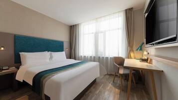 A hotel room with a bed, a desk, a chair, a TV, and a window with curtains.