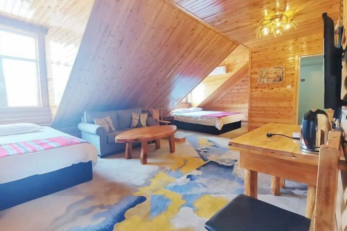 A cozy attic room with a sloped ceiling, a bed, a sofa, a small table, and a desk with a chair.