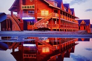 Un edificio de madera con una superficie acuática reflectante al frente, que cuenta con varios balcones y una escalera.