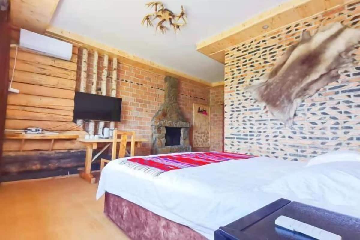 A room with a bed, a television, a fireplace, and a wooden wall.