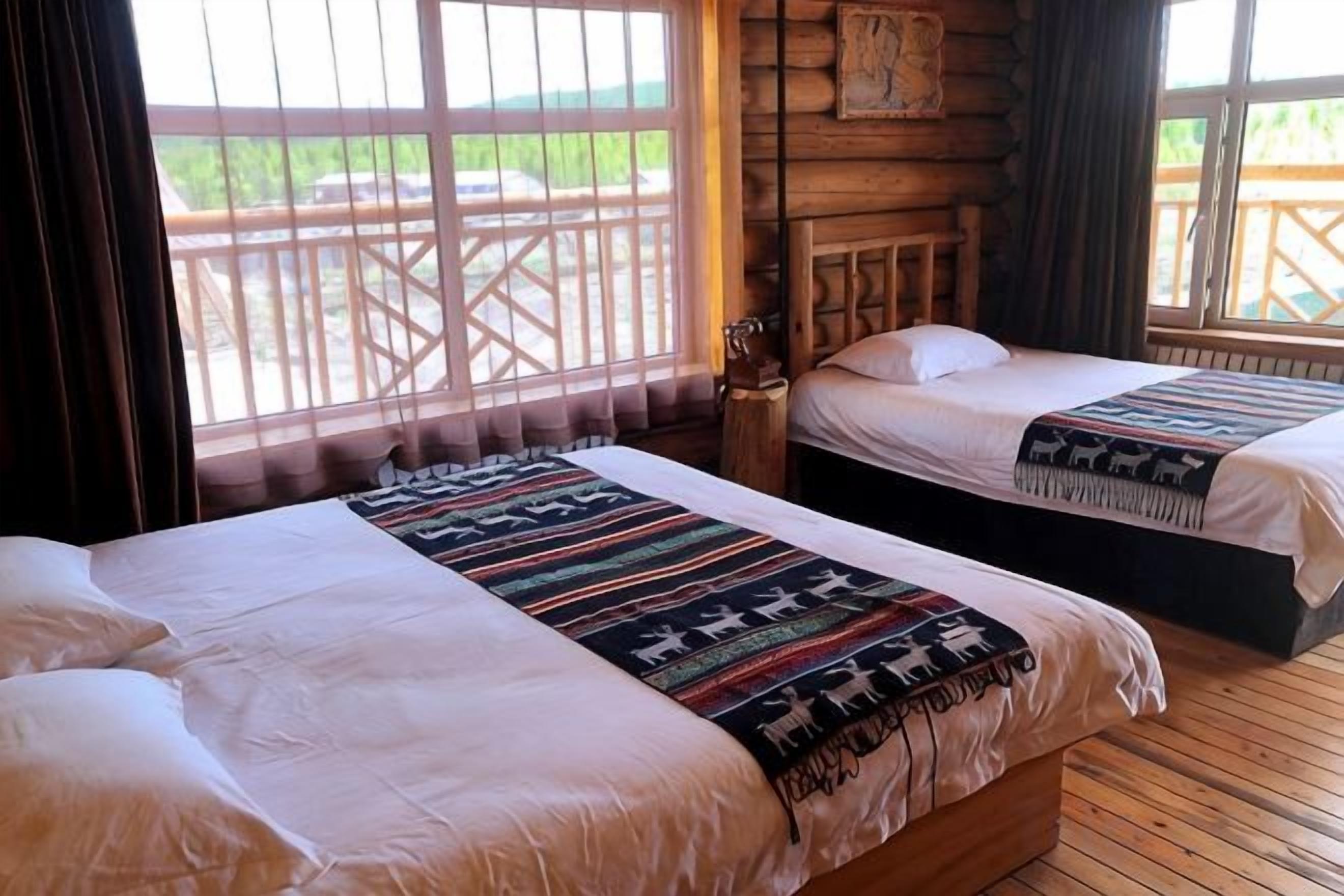 Quarto com duas camas, piso de madeira, janela com vista para um deck de madeira e decoração rústica na parede.