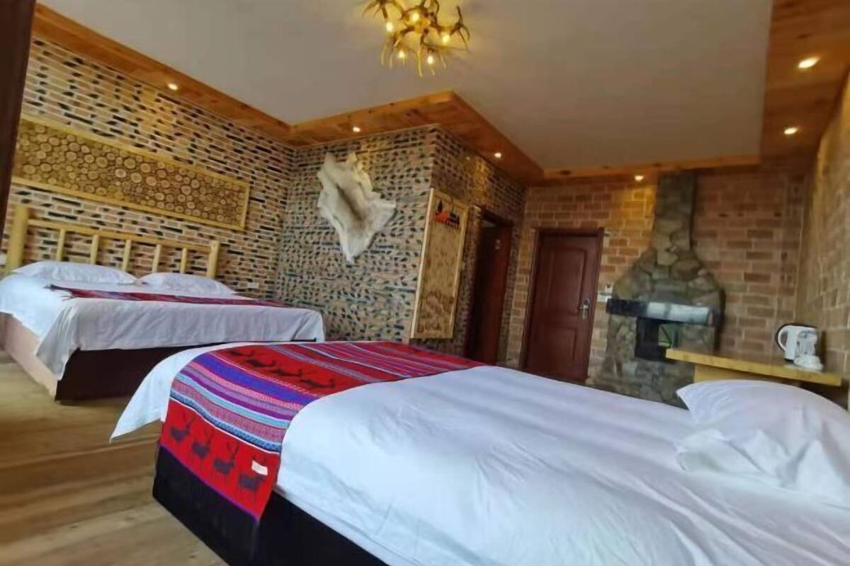 A room with two beds, a stone fireplace, and a wooden ceiling.