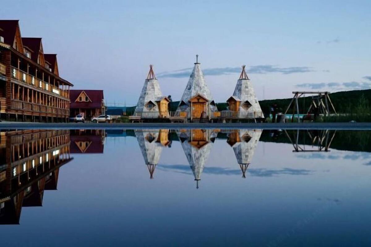 A wooden building with multiple conical roofs by a calm body of water.