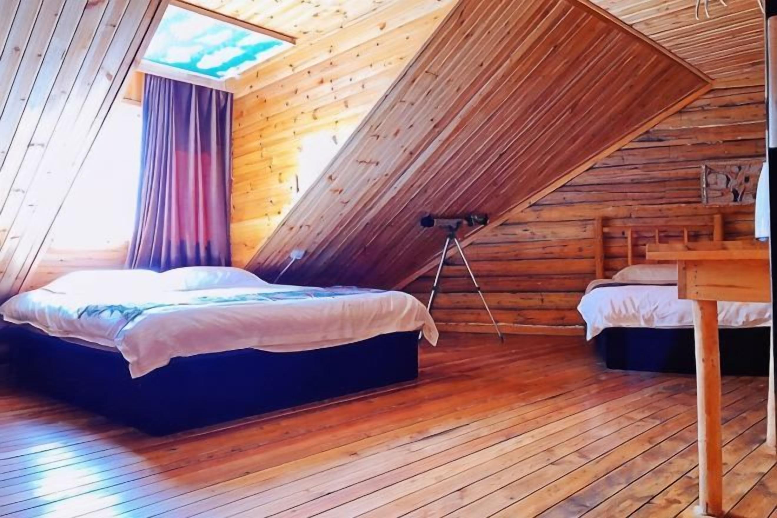 Un dormitorio con techo inclinado, una cama, una mesita pequeña y un trípode.