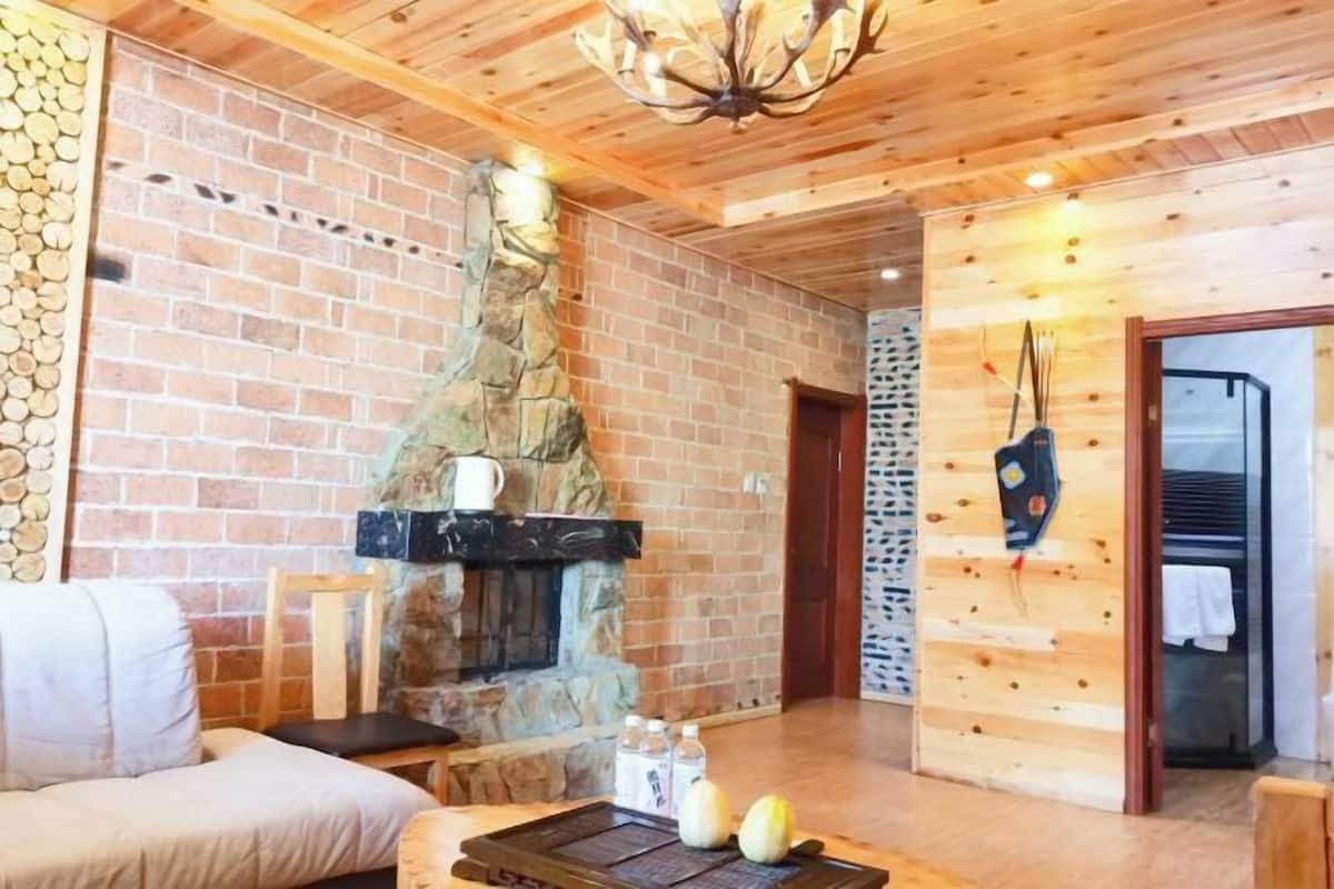 A cozy room with a stone fireplace, wooden walls, a chandelier, and a seating area.