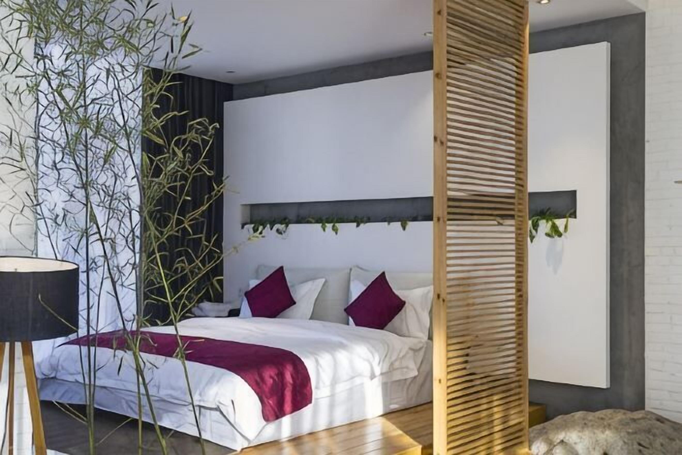A bedroom with a bed, a bedside plant, a headboard, and a wall-mounted shelf.