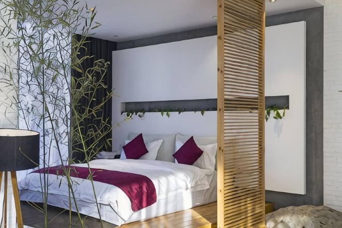 A bedroom with a bed, a bedside plant, a headboard, and a wall-mounted shelf.
