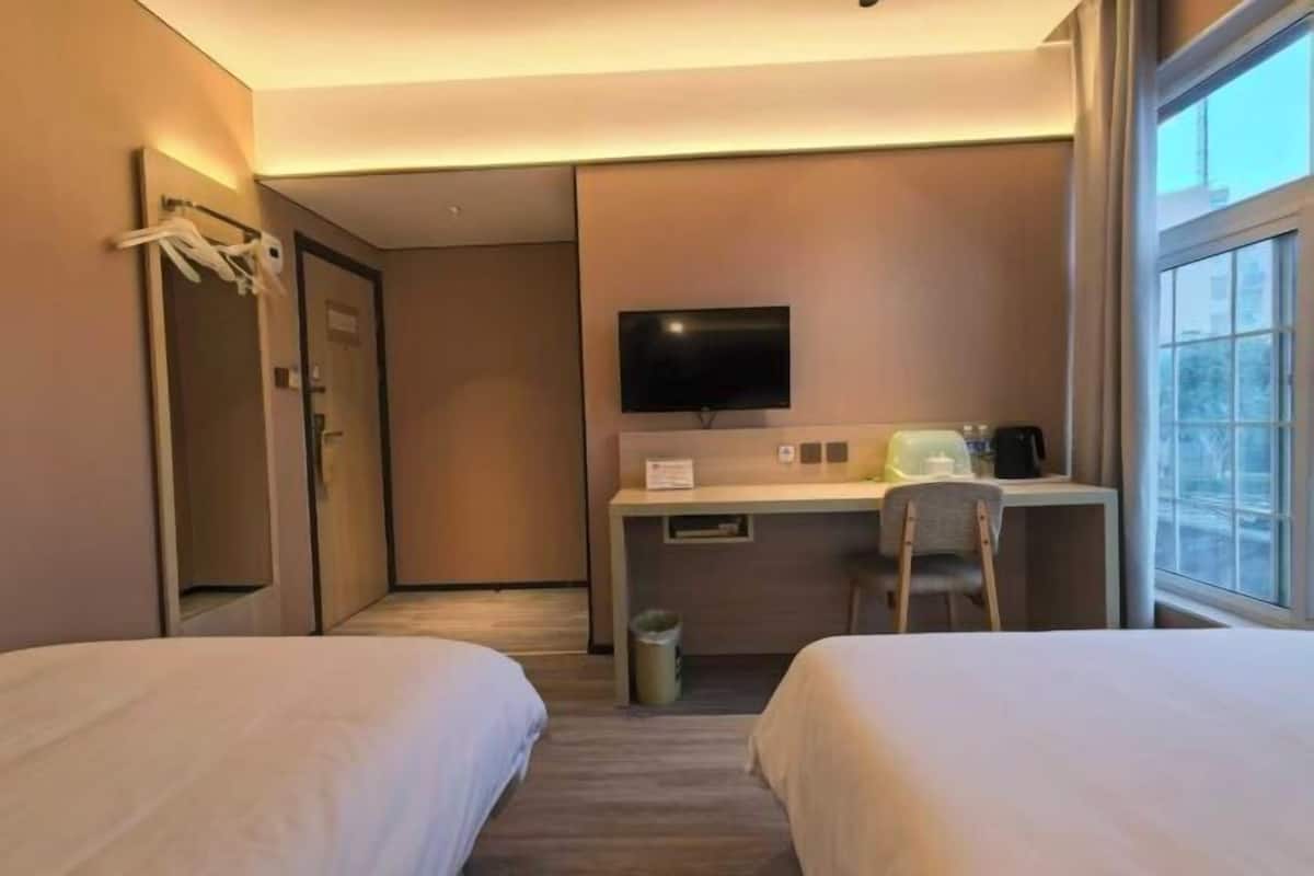 Ein Hotelzimmer mit zwei Betten, einem Schreibtisch, einem Fernseher und einem Fenster.