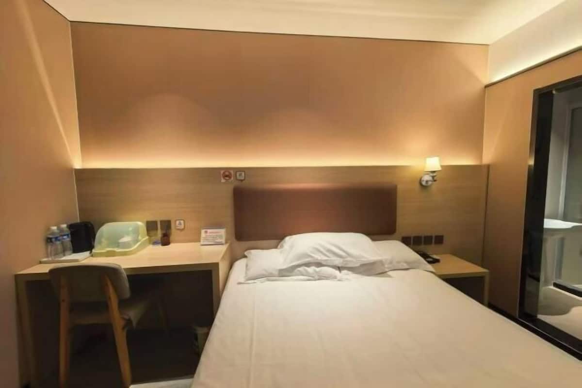 Ein Hotelzimmer mit Bett, Schreibtisch, Stuhl, Nachttisch, Lampe und Spiegel.