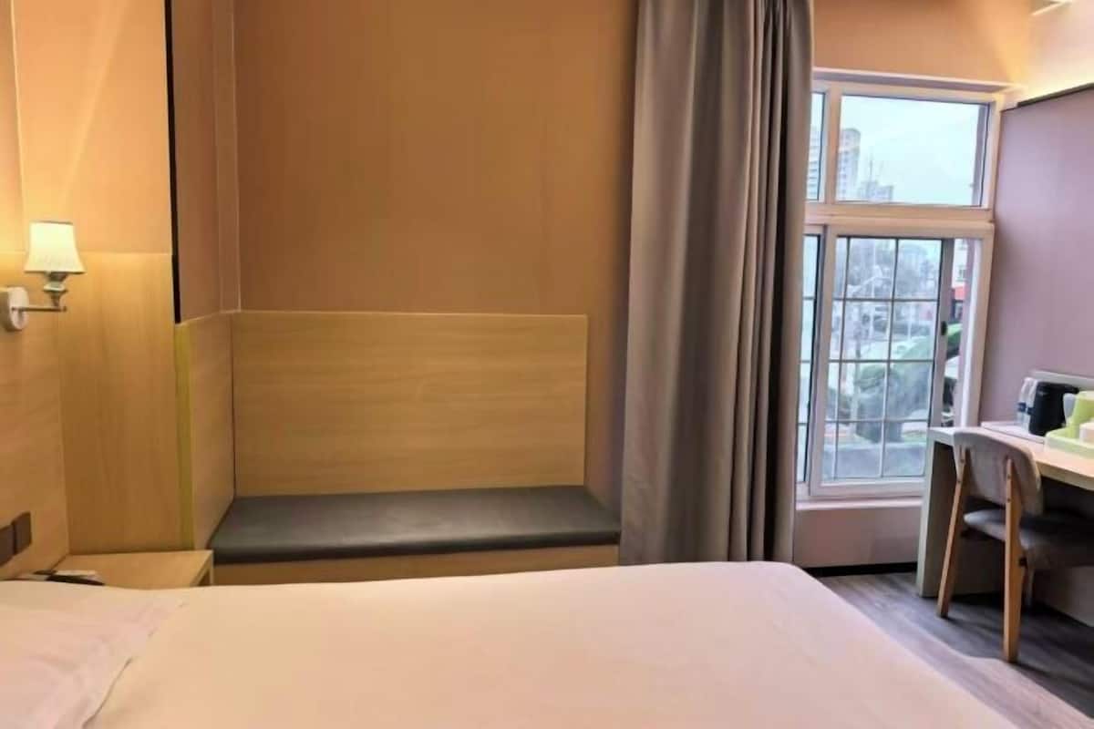 Ein Hotelzimmer mit Bett, Schreibtisch, Stuhl, Bank, Fenster und Lampe.