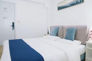 Ein ordentlich bezogenes Bett mit einer blau-weißen Tagesdecke, ein Nachttisch mit einer Vase und ein Gemälde an der Wand.