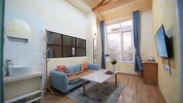 A living room with a sofa, a coffee table, a TV, and a window with curtains.
