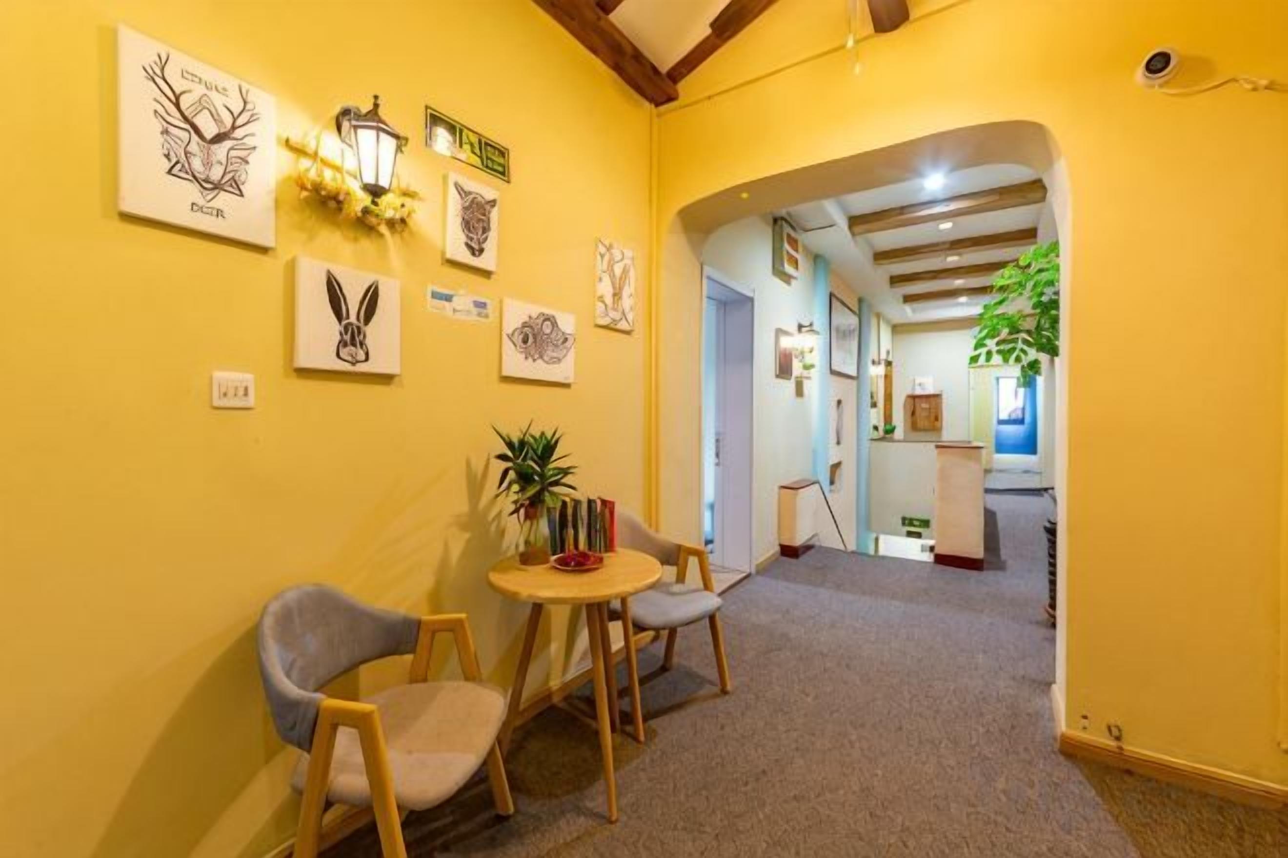 A hallway with a carpeted floor, a round table with chairs, and wall-mounted artwork.