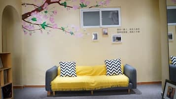 A room with a sofa, a window, a wall-mounted air conditioner, and a bookshelf.