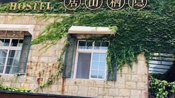 A hostel with a stone facade and green shutters, featuring a sign with Chinese characters.