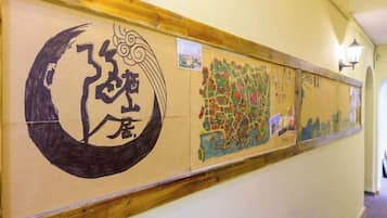 A hallway with a wooden baseboard, a wall-mounted light fixture, and a series of artworks including calligraphy and a colorful map.