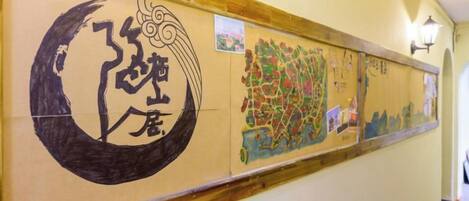A hallway with a wooden baseboard, a wall-mounted light fixture, and a series of artworks including calligraphy and a colorful map.