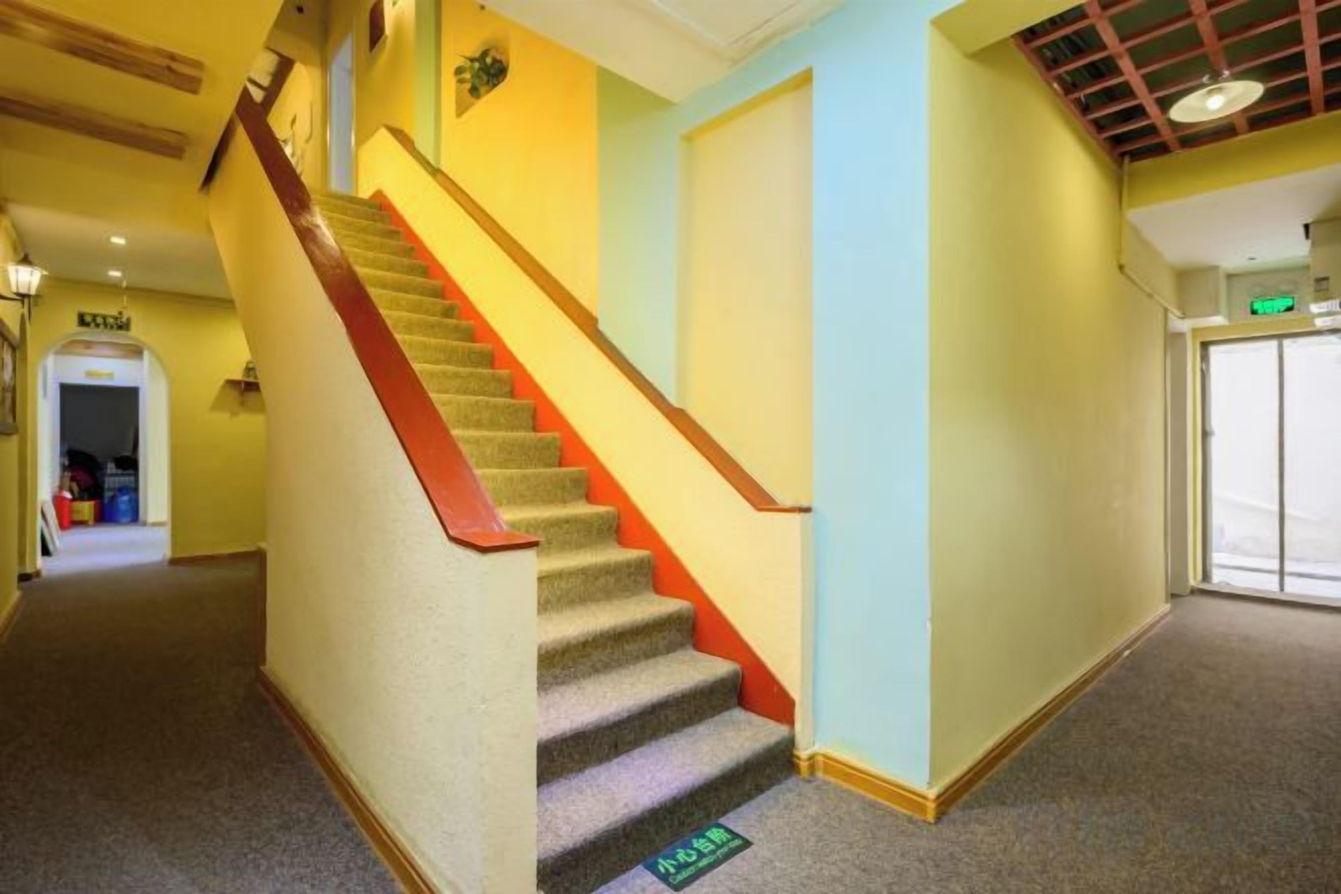 A carpeted hallway with a wooden staircase and a door with a green sign.