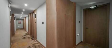 Un pasillo de hotel con puertas de madera, suelo alfombrado y un cartel que indica la dirección al ascensor.