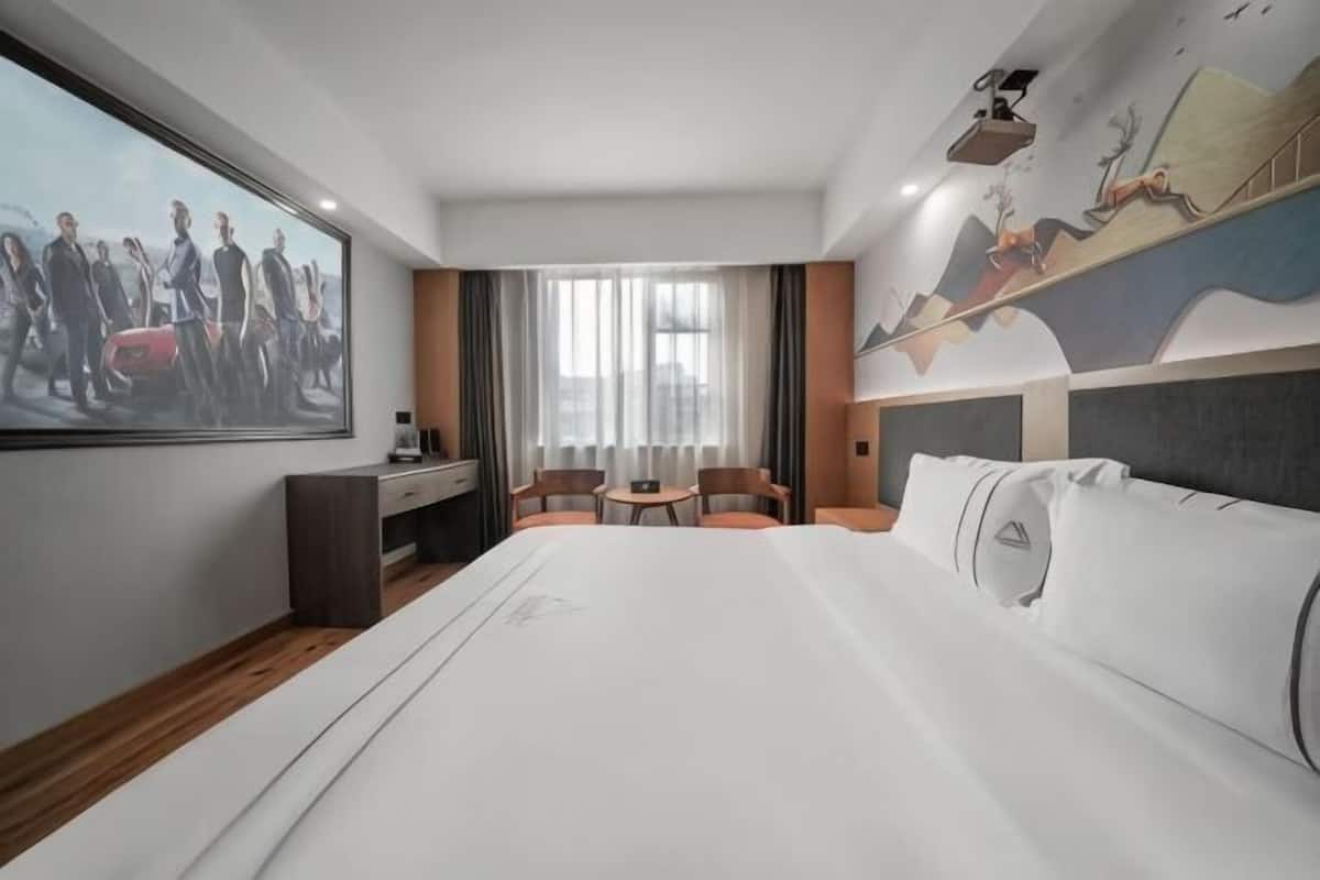 A hotel room with a large bed, a desk, a chair, a TV, and a painting on the wall.