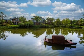 A calm lake with a boat docked on the shore, surrounded by greenery and houses. - Yingdong Resort (Shanghai)