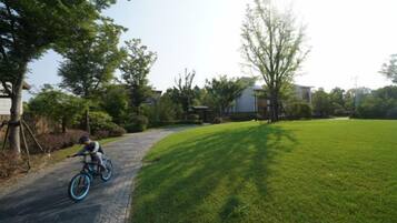 A paved driveway with a cyclist, a grassy lawn, and a residential building in the background.
