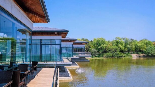 A modern building with a glass facade, wooden deck, and a view of a lake. - Yingdong Resort (Shanghai)