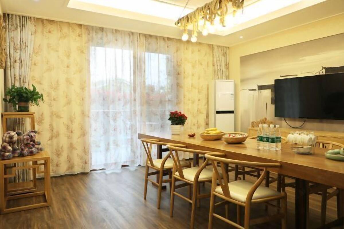 A dining area with a wooden table, chairs, a television, and a refrigerator.