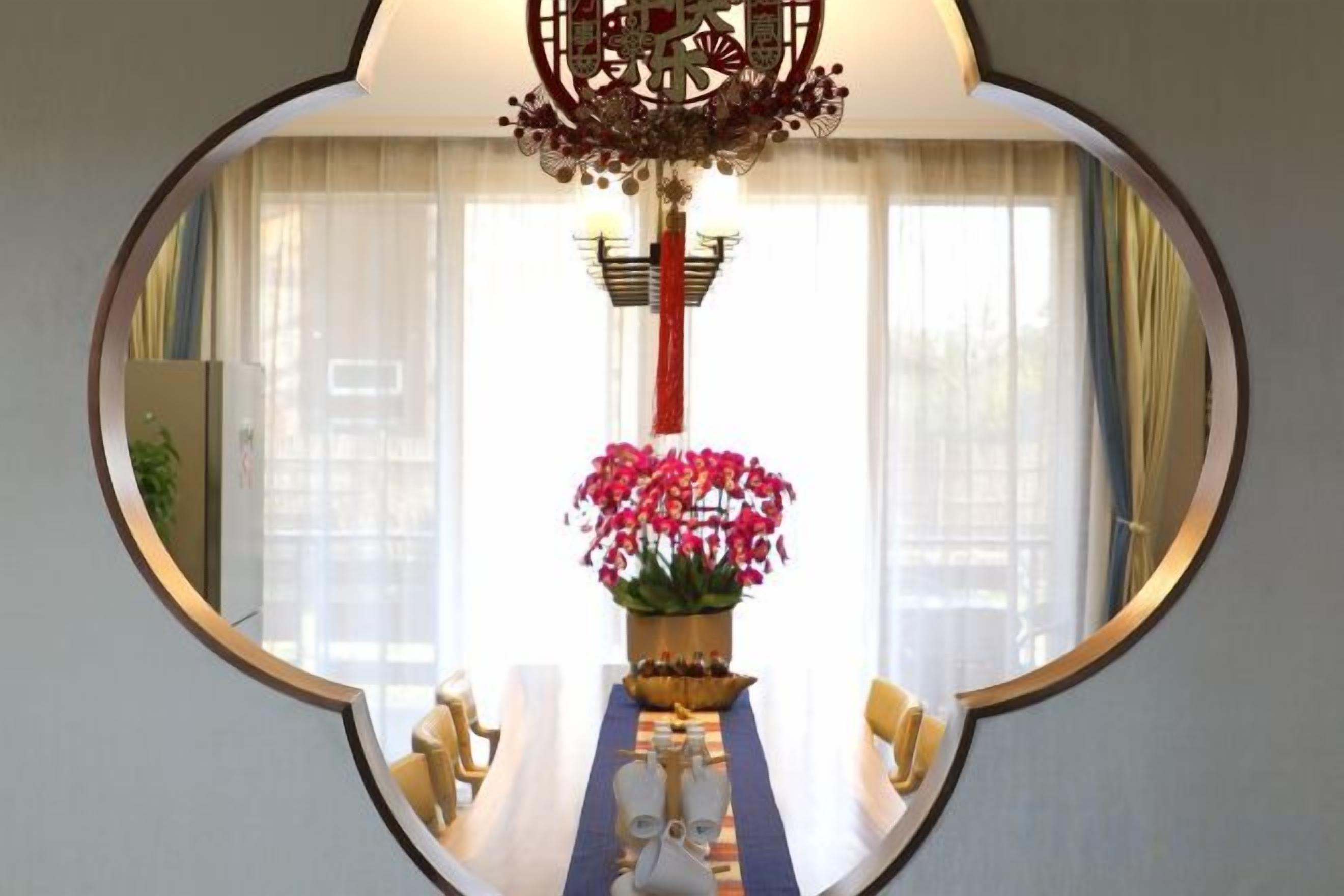 A round mirror reflecting a dining area with a table, chairs, and a vase of flowers.