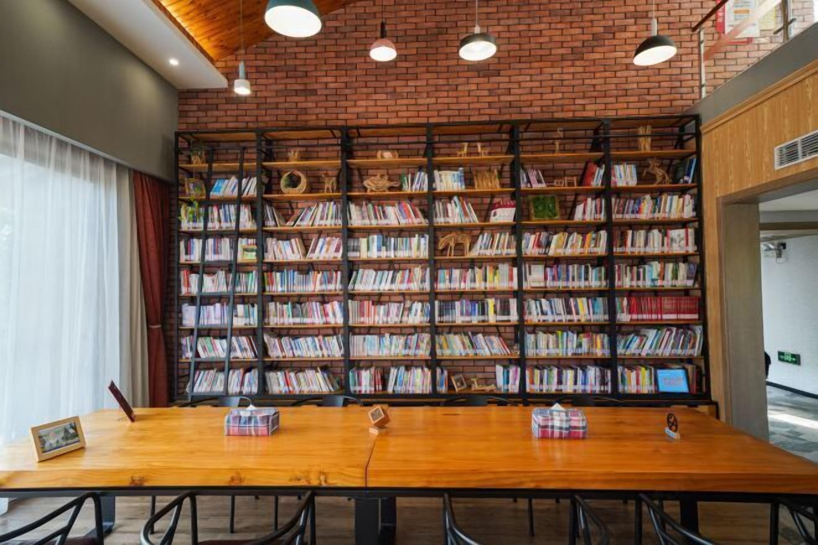 A library with a brick wall, bookshelves, and a wooden table with chairs.