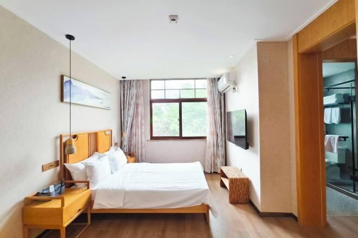 A hotel room with a bed, bedside table, TV, window, and a view of the outside.