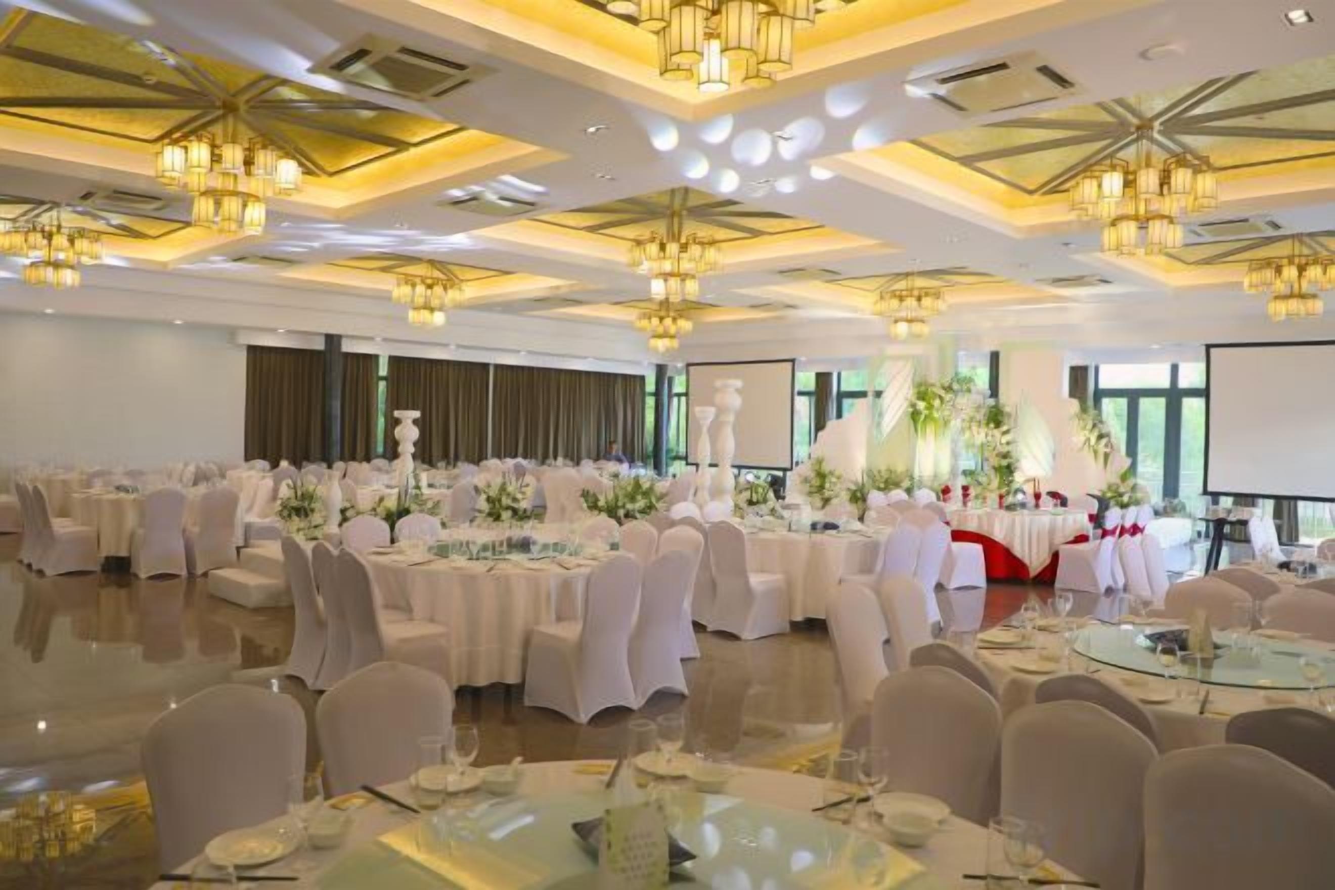 A banquet hall with round tables, chairs, and floral centerpieces.