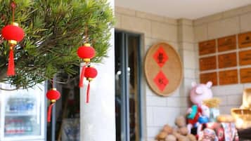 A building facade with a tree adorned with red lanterns, a wooden sign with Chinese characters, and a display of goods.