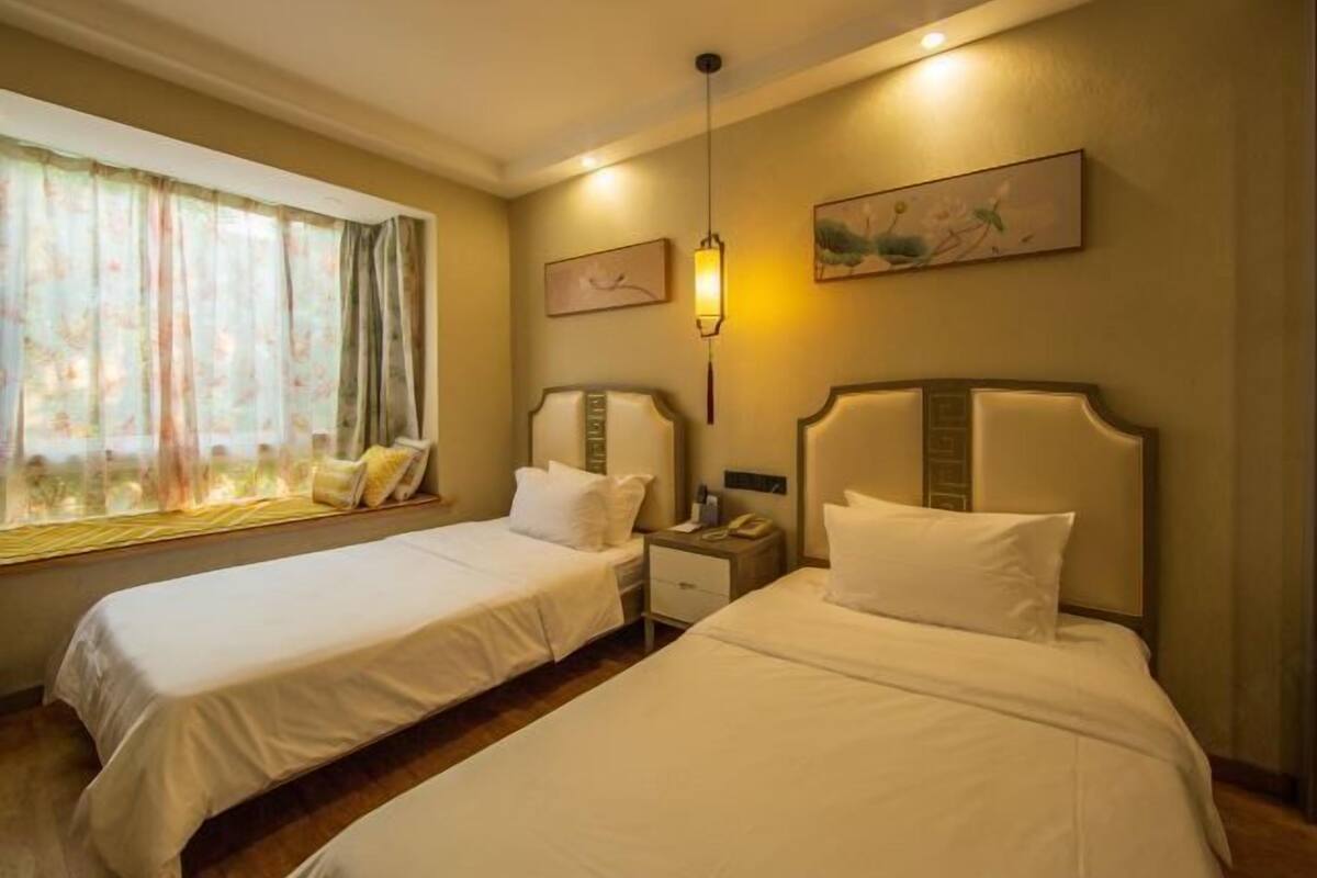 A hotel room with two single beds, a bedside table with a lamp, and a window with curtains.