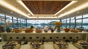 A modern dining area with a view of a lake, featuring a wooden ceiling, pendant lighting, and buffet stations. - Yingdong Resort (Shanghai)