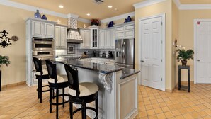 A kitchen with white cabinets, a stainless steel refrigerator, and a marble island with bar stools.