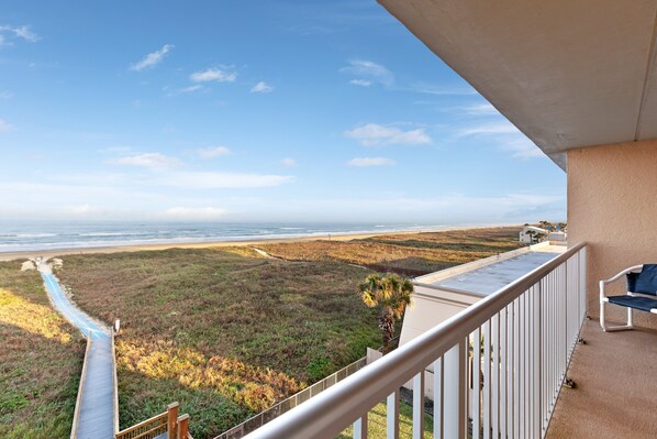 A balcony with a view of the beach and a path leading to the water.