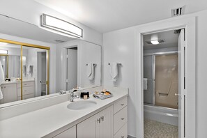A modern bathroom with a large mirror, white vanity, and a shower area.