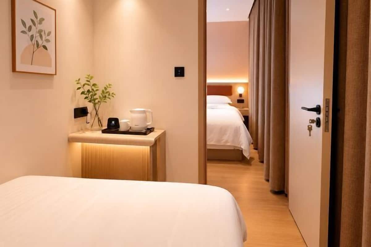 A hotel room with a bed, bedside table with a plant, and a nightstand with a coffee maker.