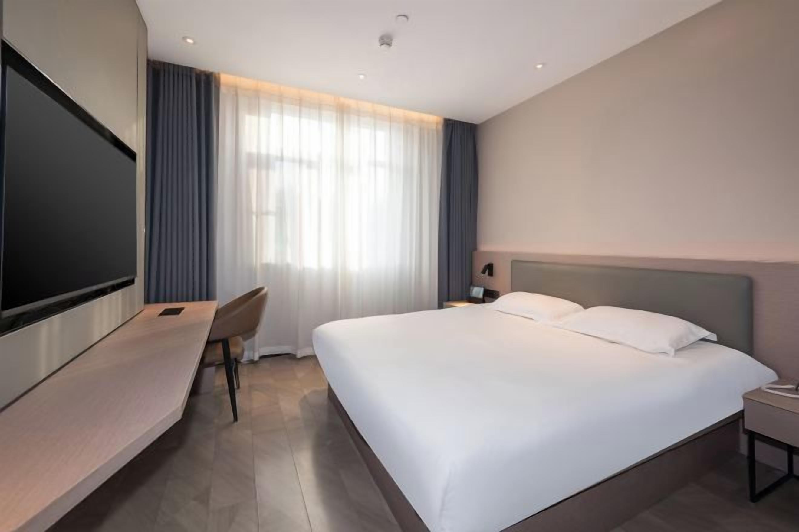 Habitación de hotel con cama, escritorio, televisor y ventana con cortinas.