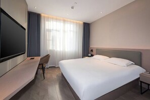 Habitación de hotel con cama, escritorio, televisor y ventana con cortinas.