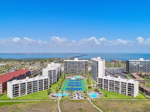 A high-rise hotel with multiple balconies, a central pool area, and a view of the ocean.