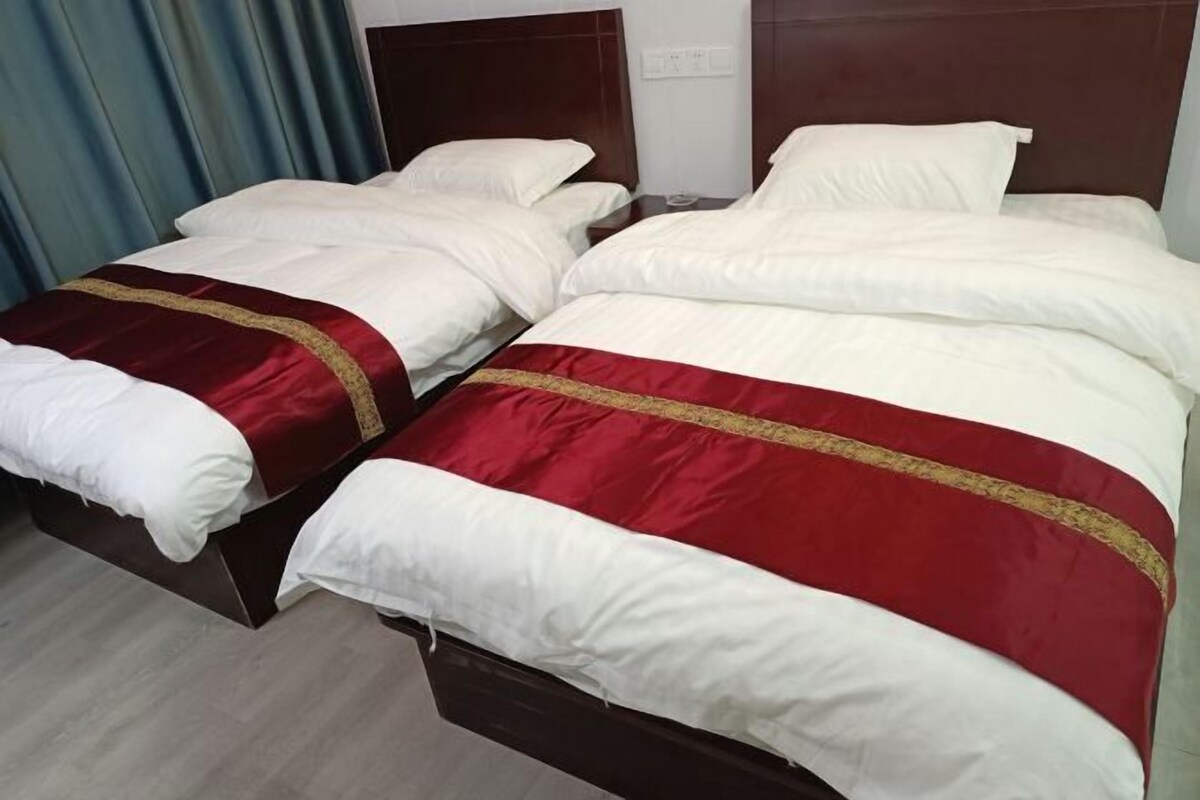A double bed with white and red bedding, a wooden headboard, and a wooden floor.