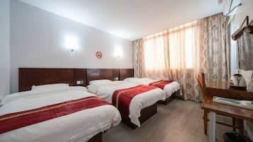 Quarto de hotel com duas camas, uma escrivaninha, uma cadeira, um bule e uma luminária na parede.
