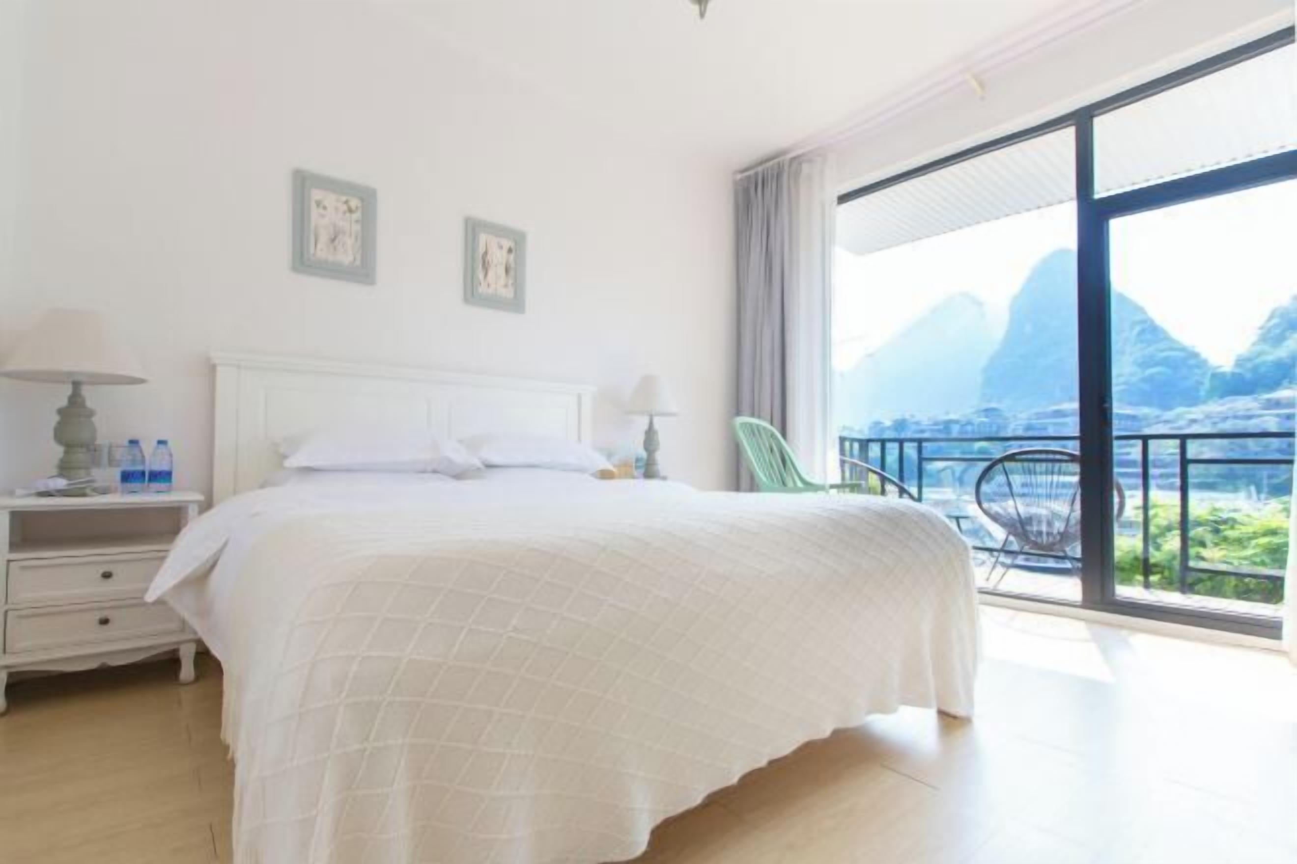 Une chambre dotée d’un grand lit, d’une table de chevet, d’une chaise et offrant une vue sur les montagnes depuis un balcon.