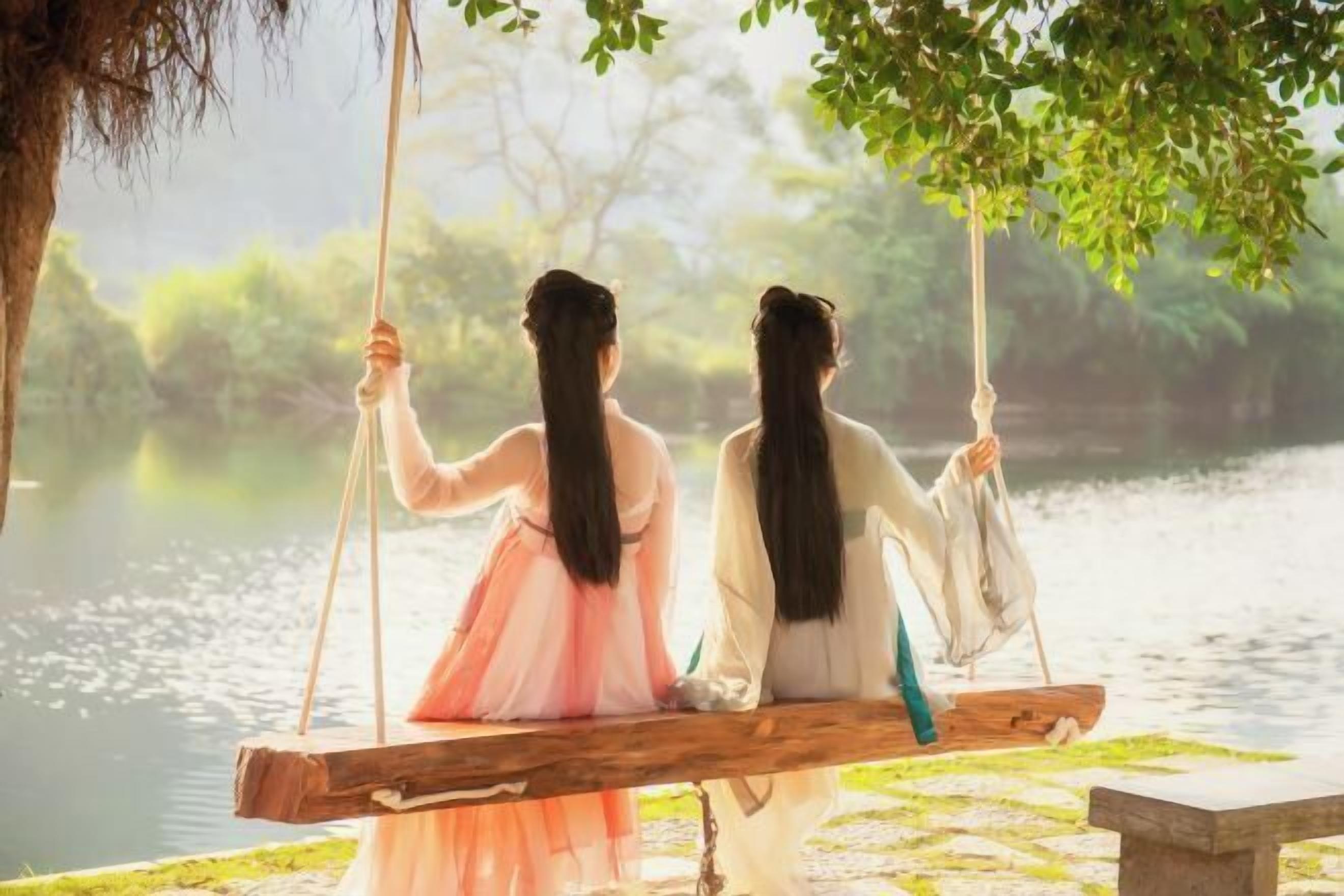 Two individuals on a swing overlooking a body of water with trees in the background.