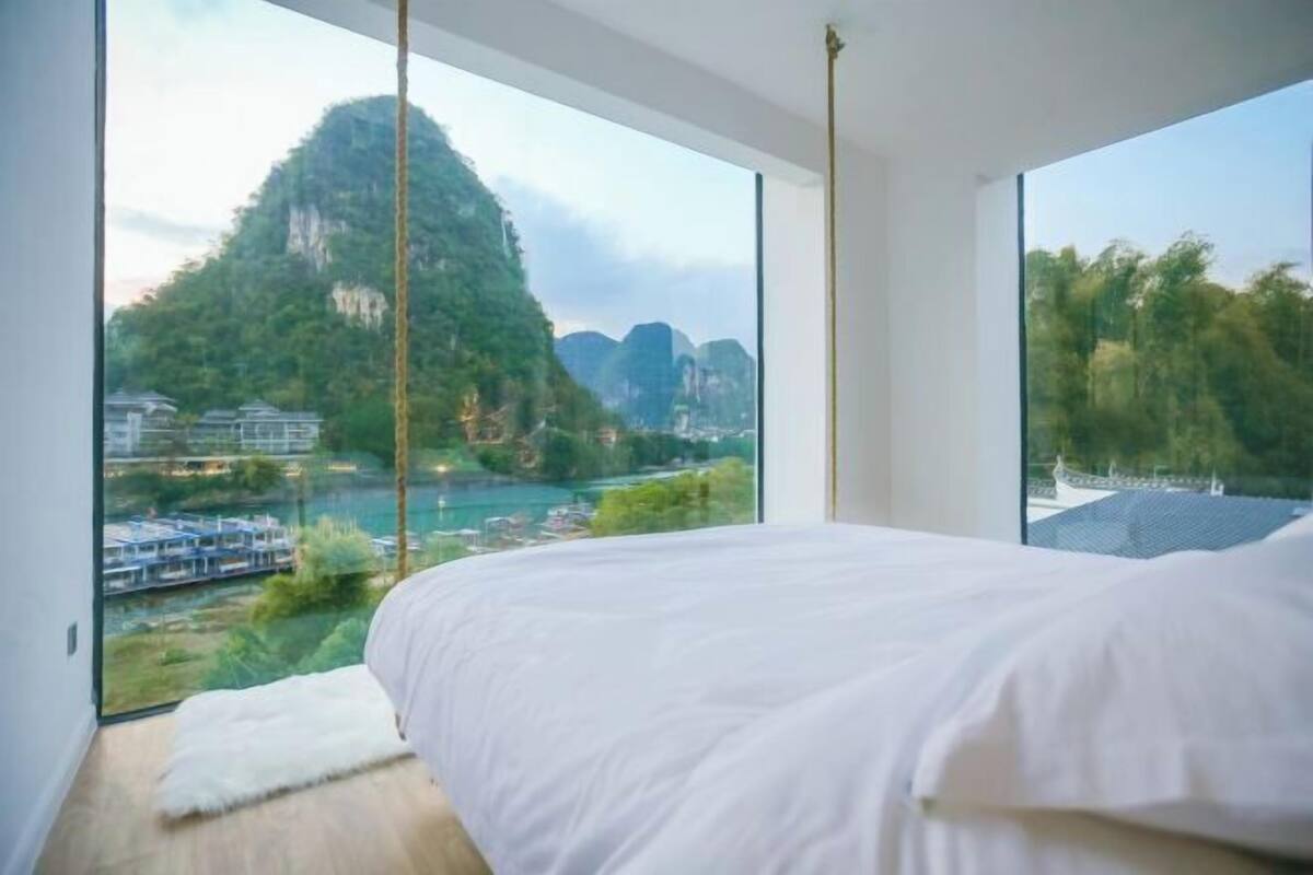 A bedroom with a large bed, a view of a mountainous landscape, and a river.