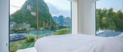 A bedroom with a large bed, a view of a mountainous landscape, and a river.