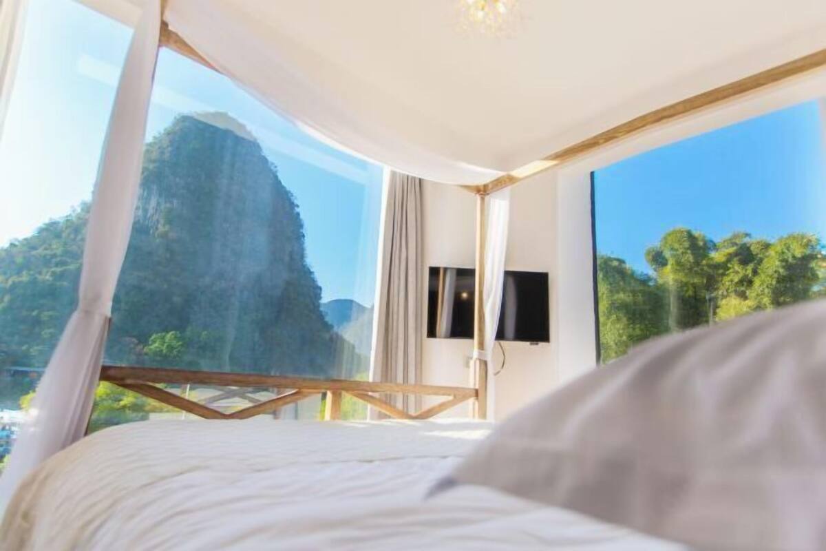 A bedroom with a bed, a TV, and large windows offering a view of a mountain and trees.