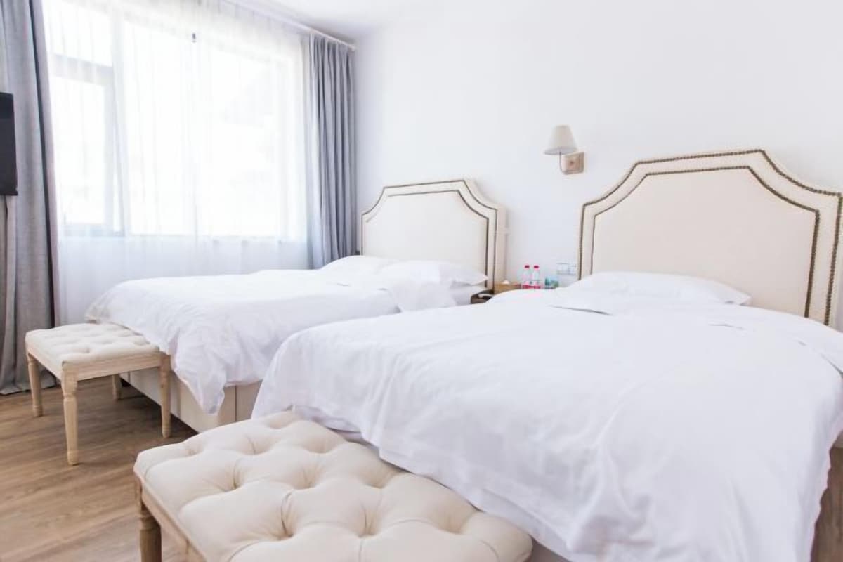 Habitació d'hotel amb dos llits, una banca, una taula de nit i una finestra amb cortines.
